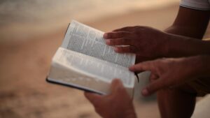 Close-up of hands holding an open Bible on a beach, symbolizing faith and study.